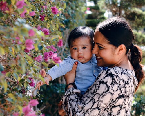 Улыбающаяся мама несет своего милого мальчика возле цветущих цветов