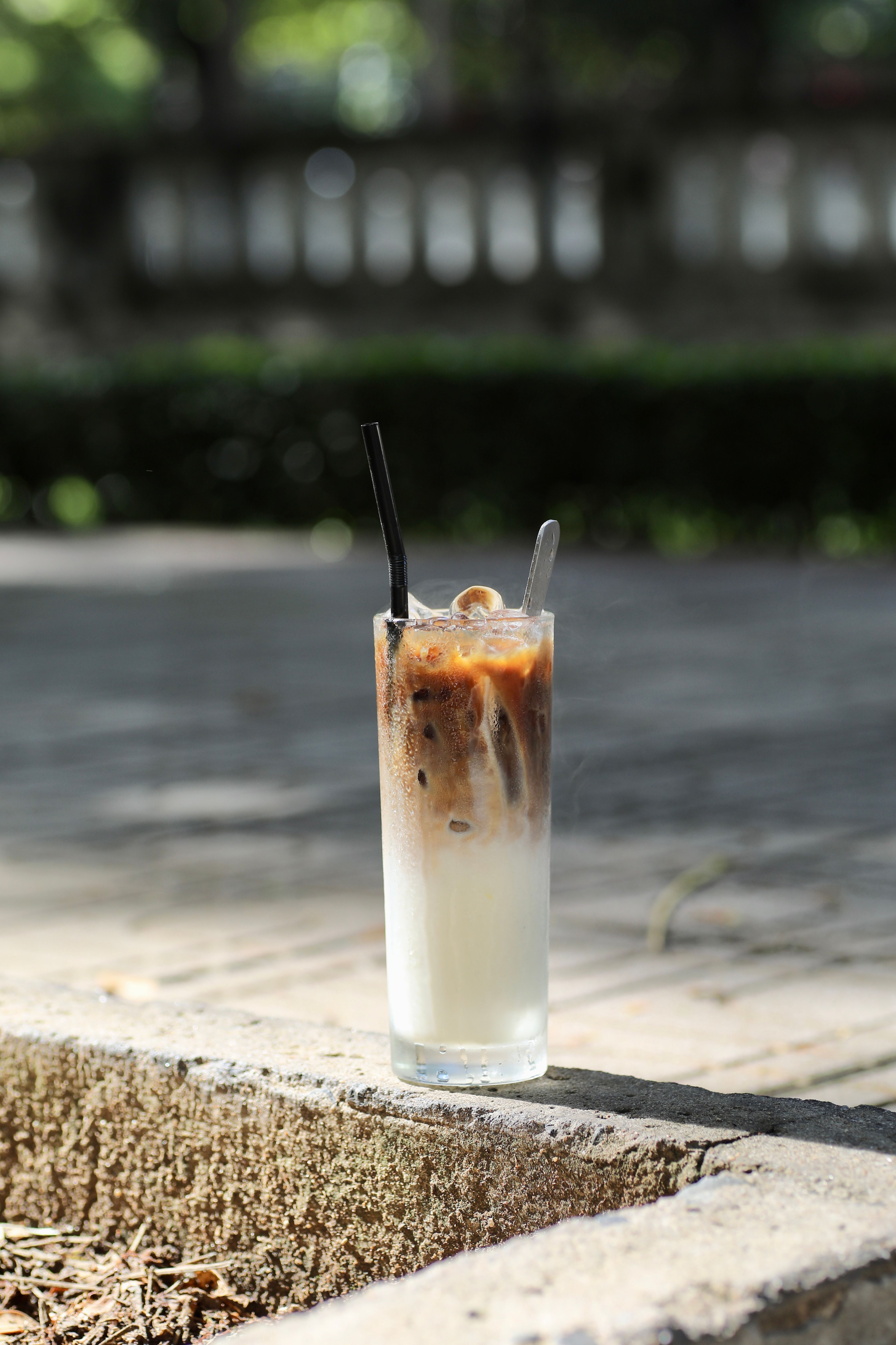 Tall iced coffee latte with straws, enjoyed outdoors on a sunny day.