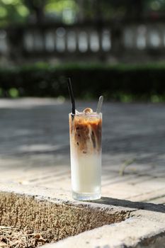Tall iced coffee latte with straws, enjoyed outdoors on a sunny day.