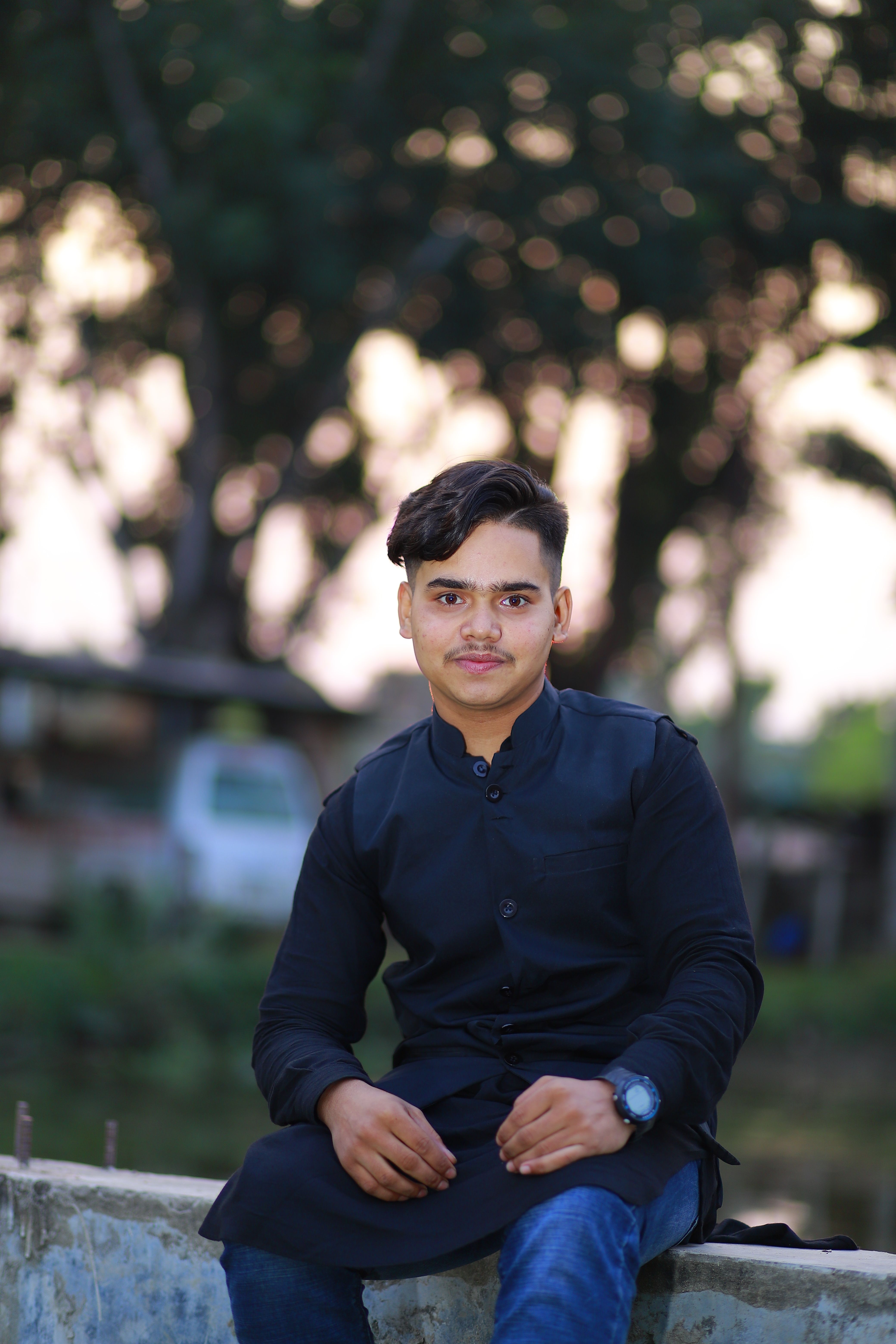 Portrait of a young man sitting outdoors with a blurred natural background.