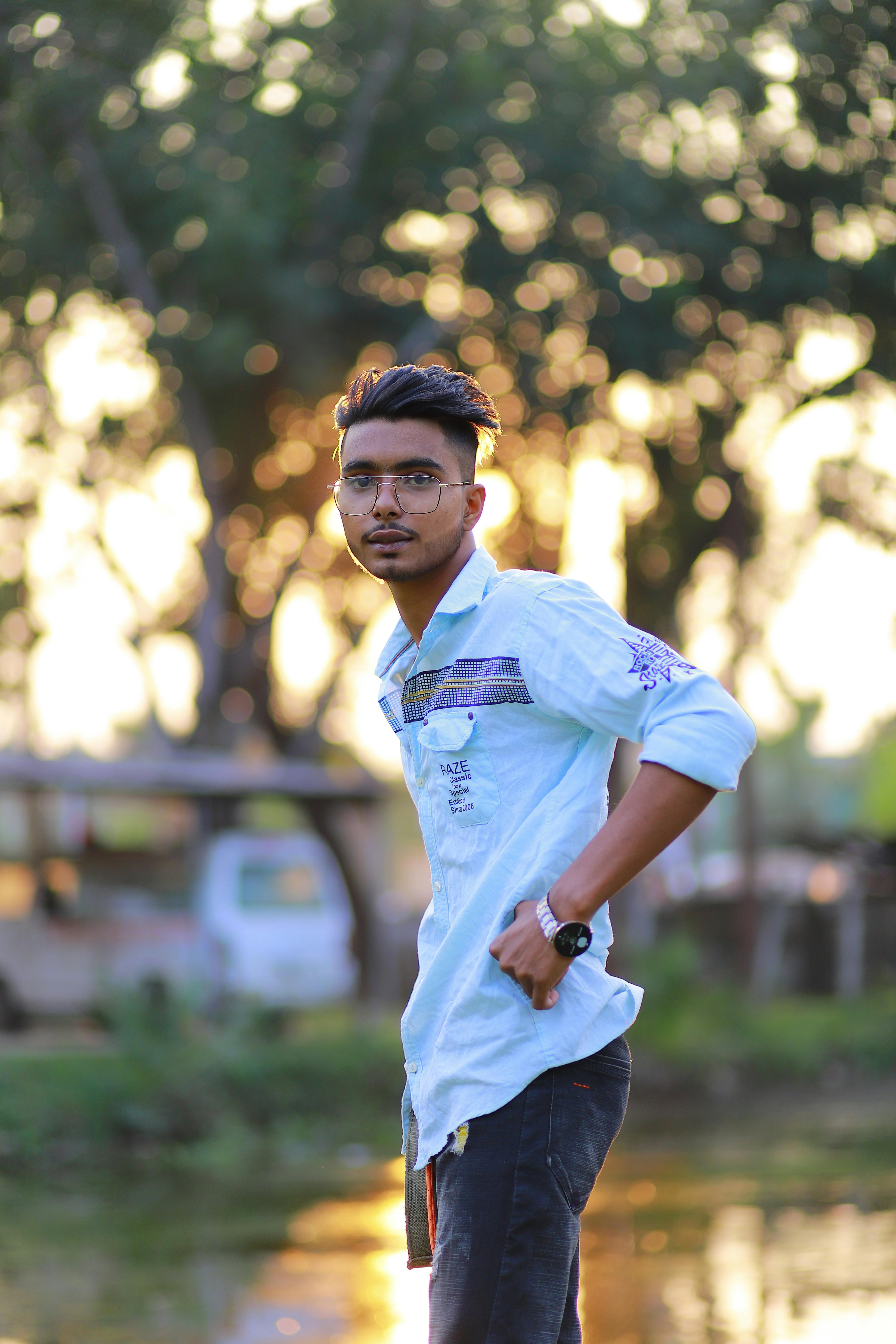 A young man outdoors in Bangladesh, dressed casually, with a sunlit background and trees.