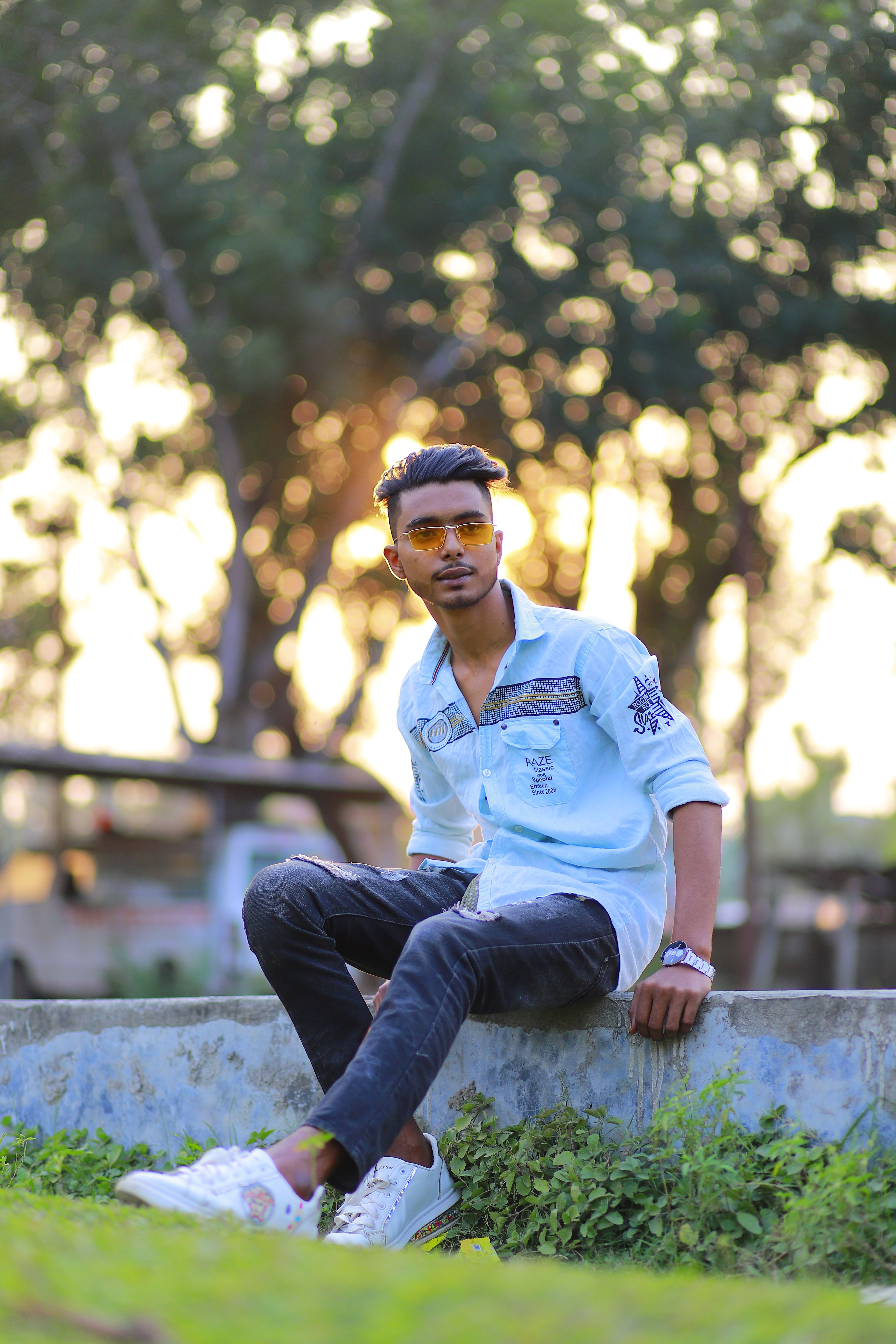 Fashionable young adult with sunglasses posing in a park setting in Bangladesh.