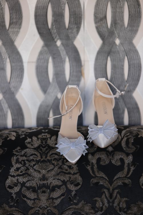 Free Stylish white heels with bows set against a patterned backdrop, perfect for weddings and formal events. Stock Photo