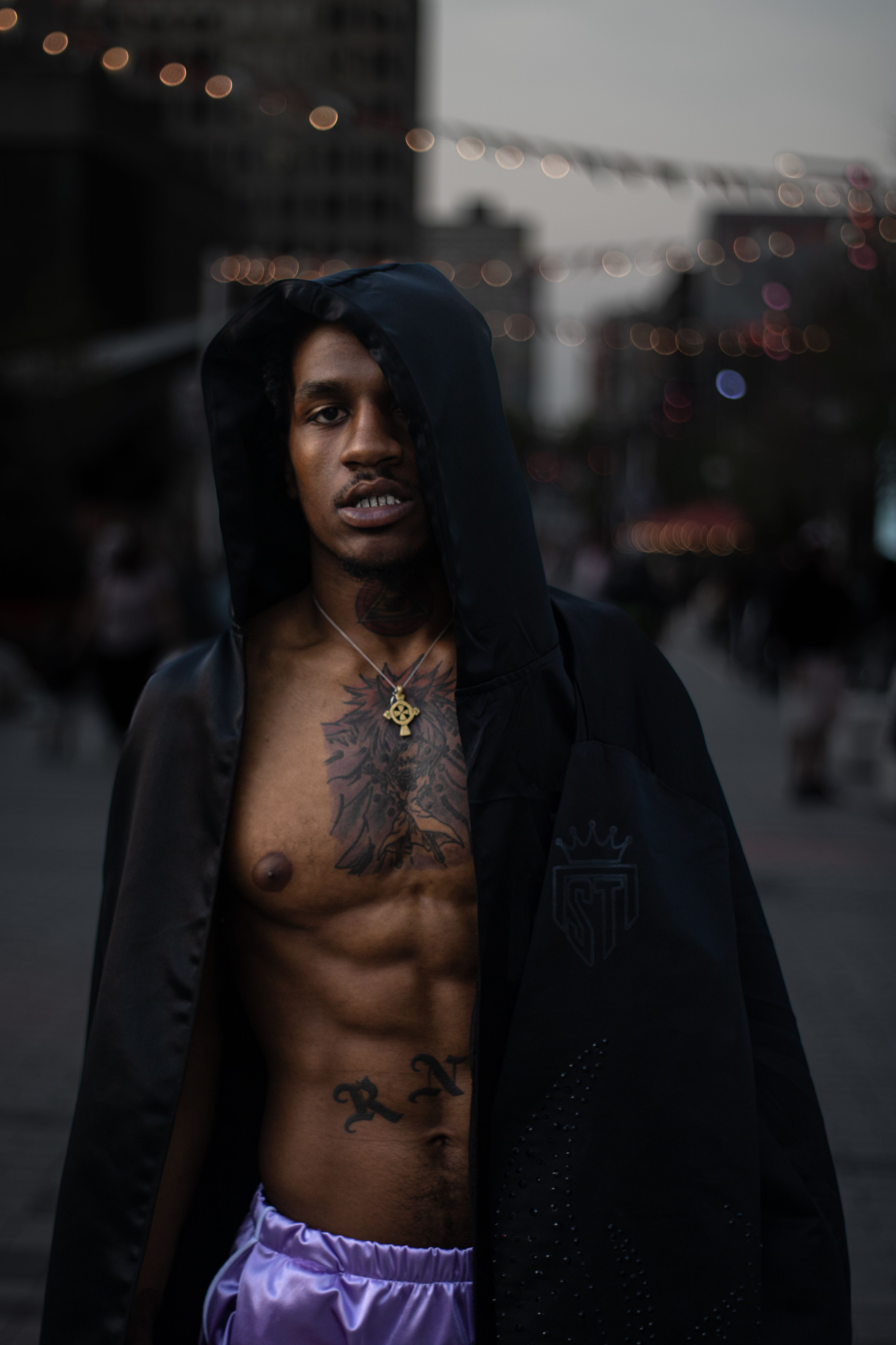 A dramatic night portrait of a hooded man in downtown Montreal with city lights.