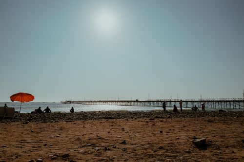 Free A sunny day at Pacasmayo Beach in Peru, featuring a vibrant orange umbrella and distant pier. Stock Photo