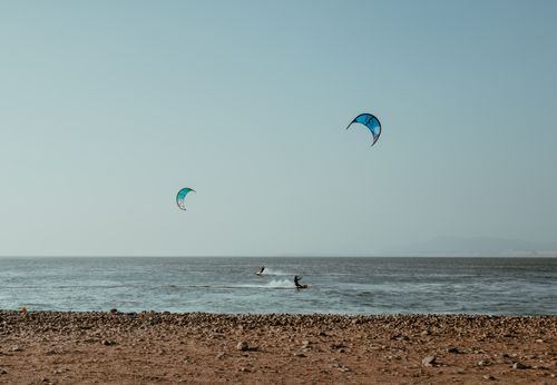 Free Two kitesurfers glide over the waves off the rocky beach of Pacasmayo, Peru. Stock Photo