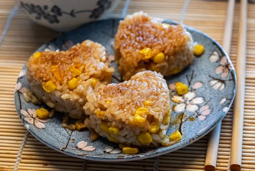 Heart-shaped grilled rice balls with corn on a floral plate, perfect for a cozy meal or snack.