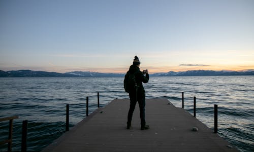 Person Standing on a Dock While Taking Photo of a Lake