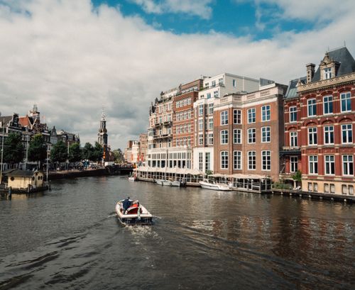 Free Charming view of boats navigating an Amsterdam canal featuring iconic Dutch architecture. Stock Photo