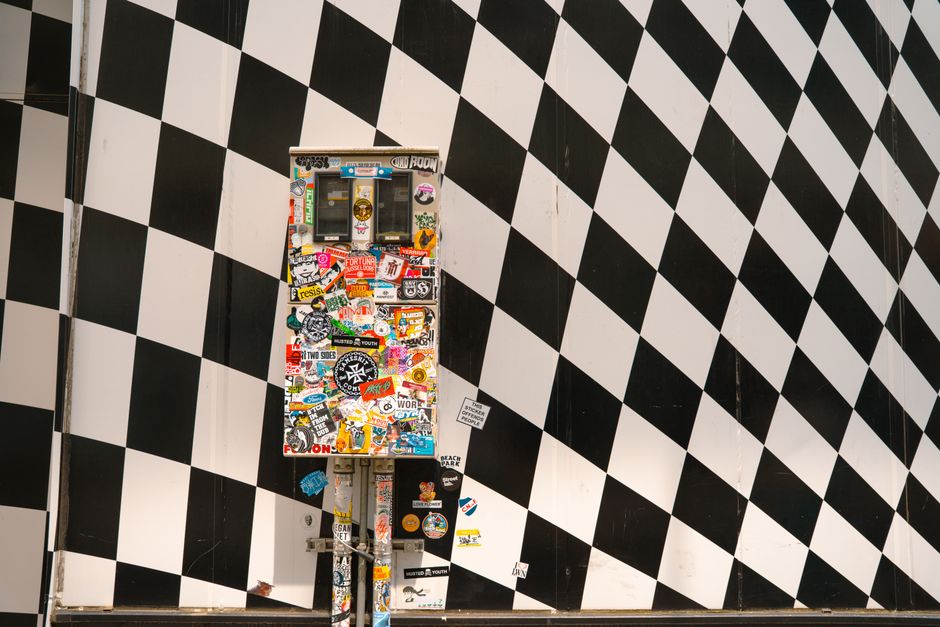 A colorful sticker-covered utility box against a black and white checkered wall in Tokyo.