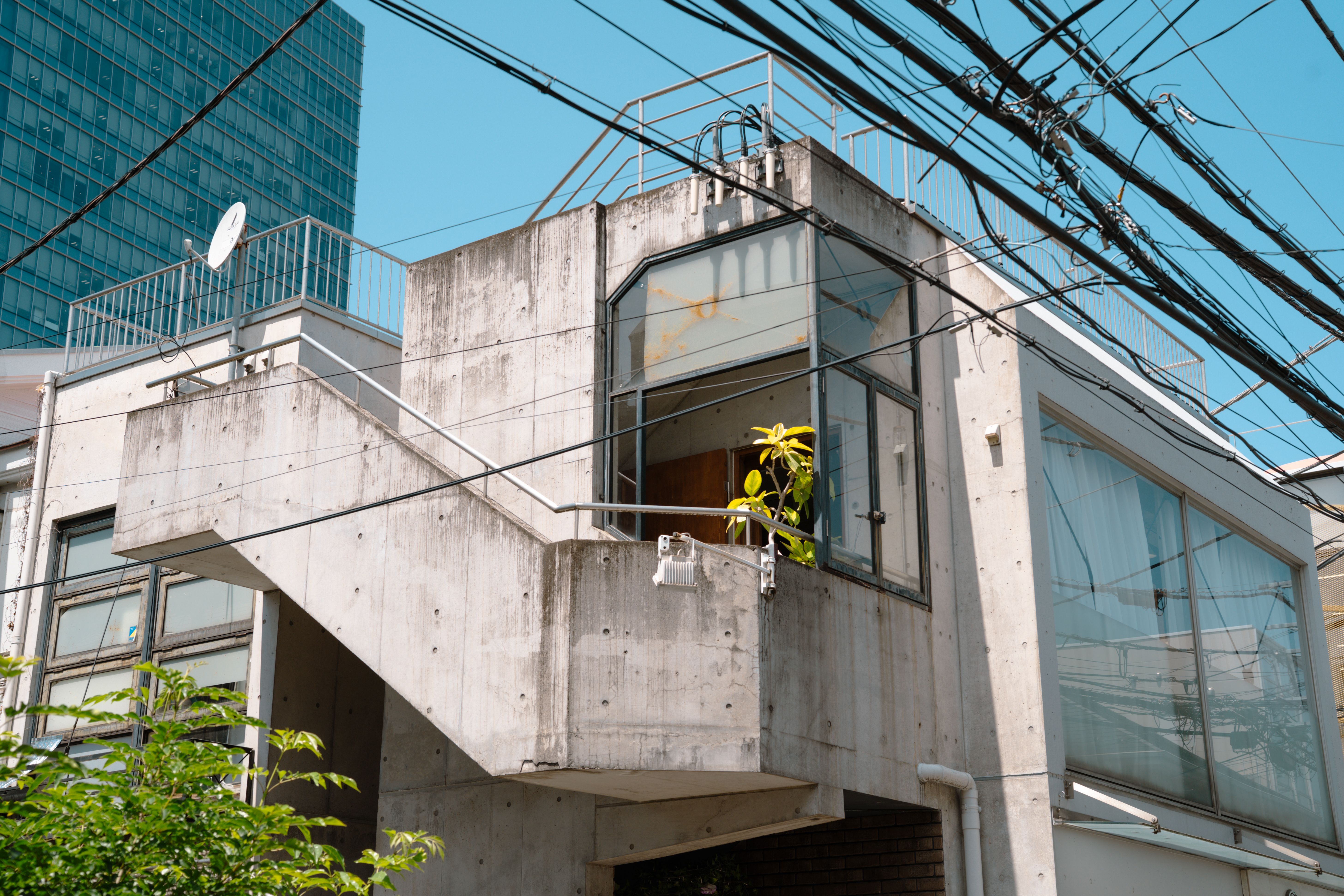 A modern concrete home in Tokyo with rooftop decking, blending urban and minimalist styles under clear skies.