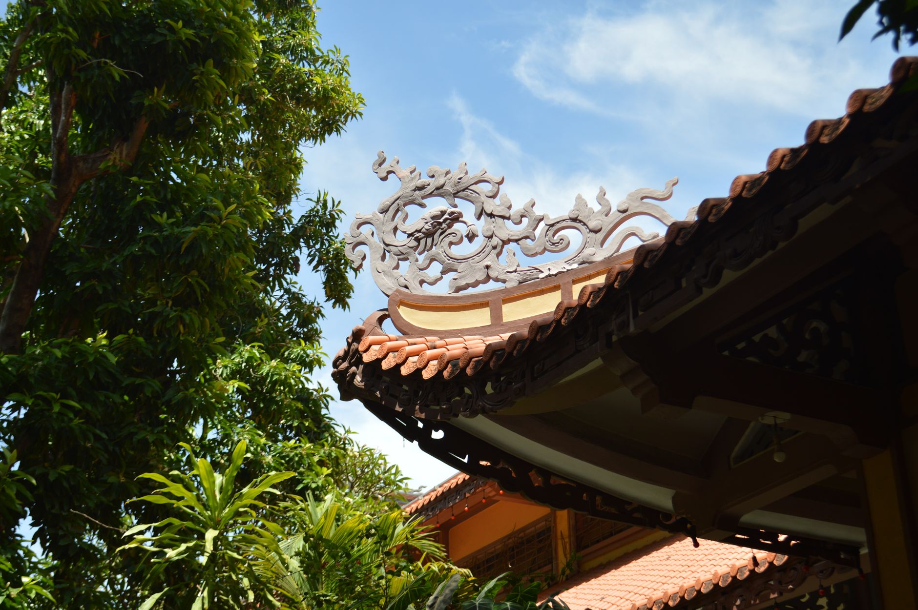 Intricate roof design on a traditional Asian building surrounded by lush greenery under a clear sky.