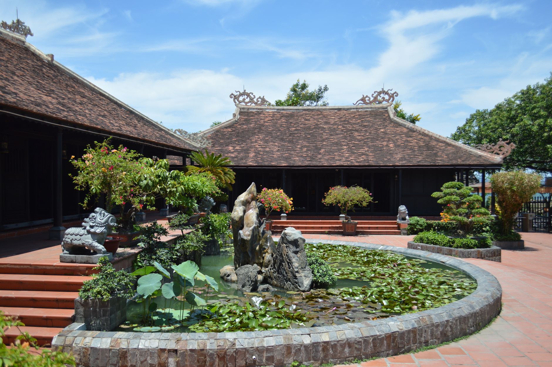 Tranquil Asian garden featuring a pond, ornate roofing, lush greenery, and intricate sculptures.