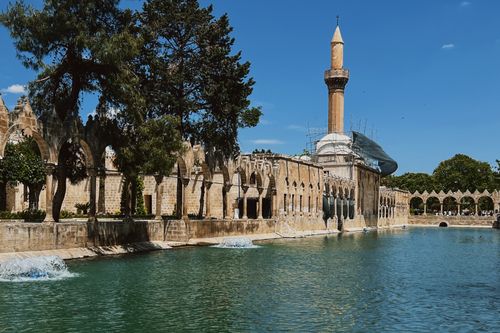Free A stunning view of a historic mosque beside a reflecting pool under a clear blue sky in Şanlıurfa. Stock Photo