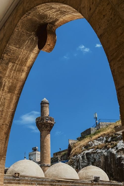 Free Historic minaret seen through a stone archway against a clear blue sky. Stock Photo