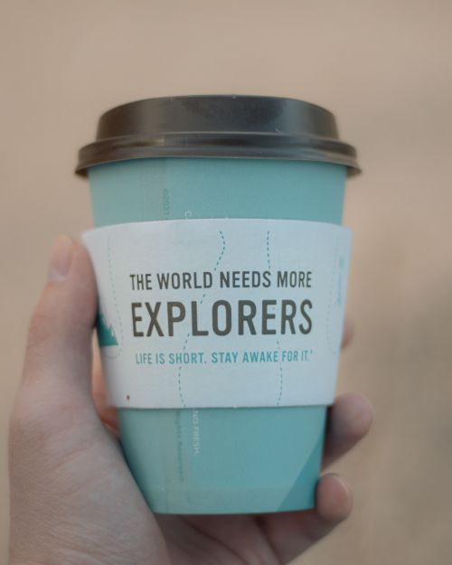 Free A hand holds a coffee cup with a motivational message about exploration. Stock Photo