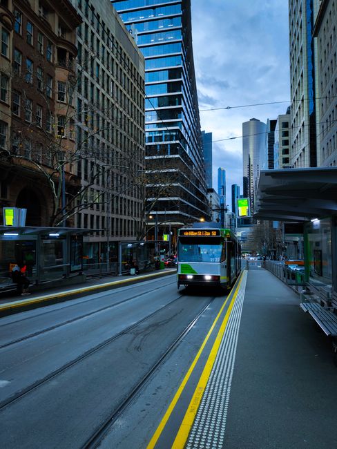 Tram moving through Melbourne's bustling city center, surrounded by modern architecture and urban life.