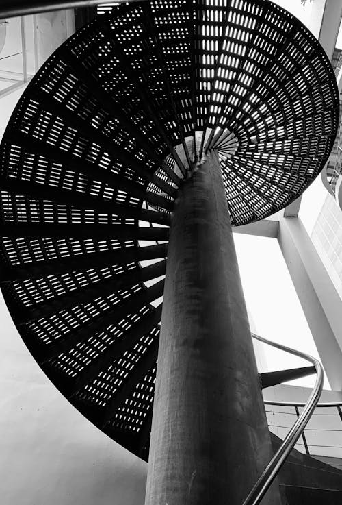 From below of black and white spiral staircase with metal railings inside modern building on daytime
