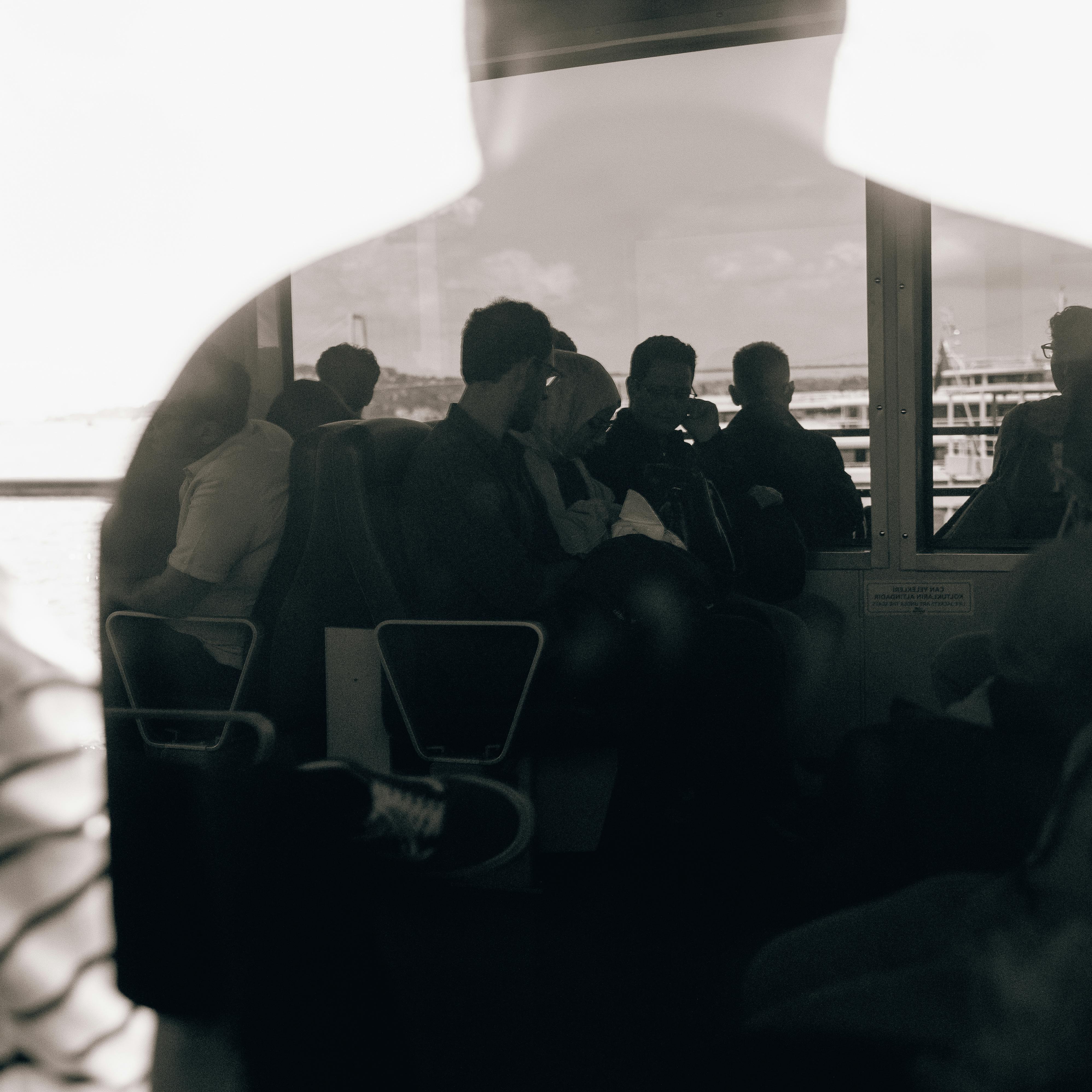 Silhouetted passengers on an Istanbul ferry captured through a reflective window, in black and white.