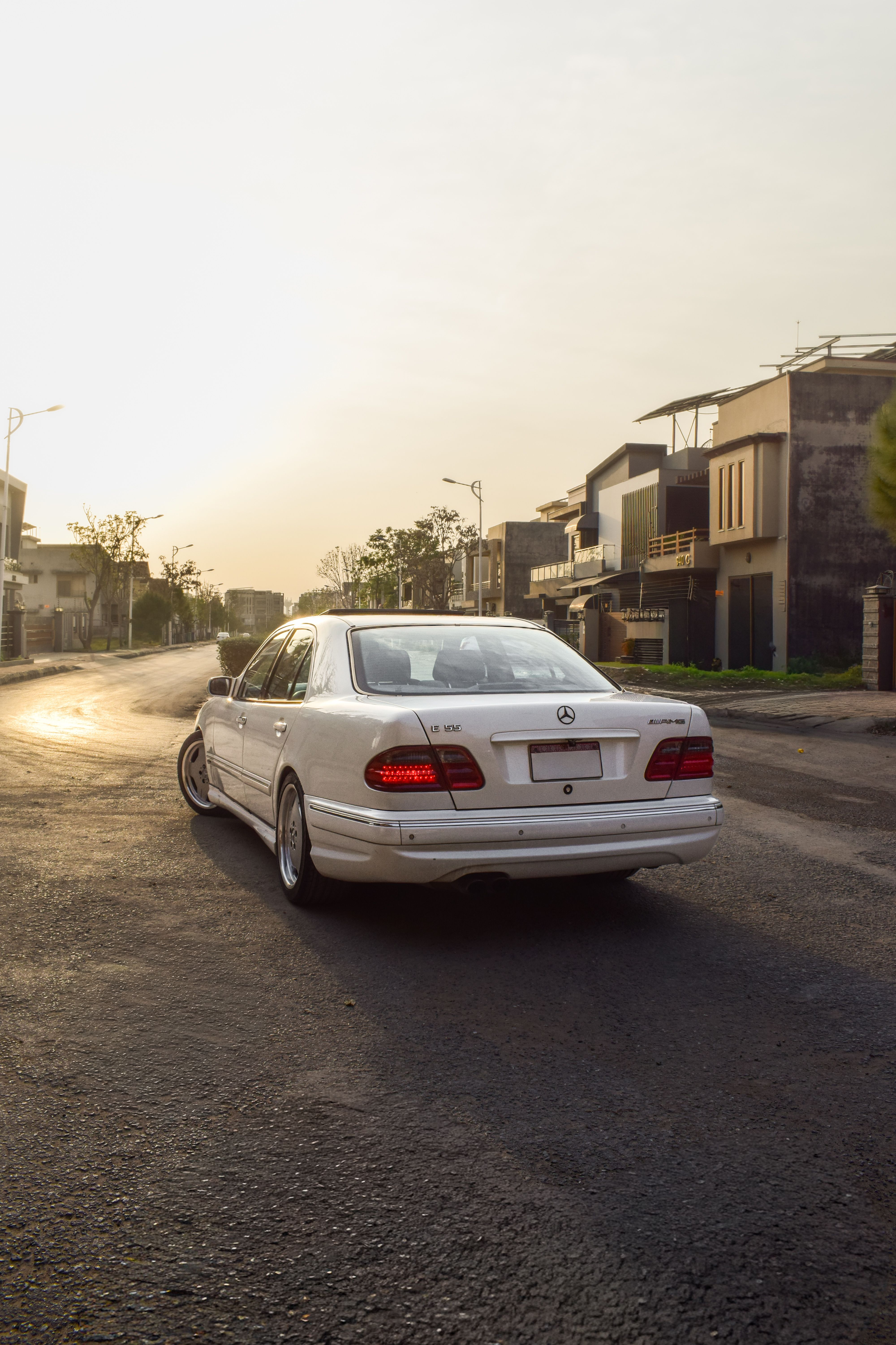 A white Mercedes Benz driving through a suburban street in Rawalpindi during sunrise, showcasing calm urban life.