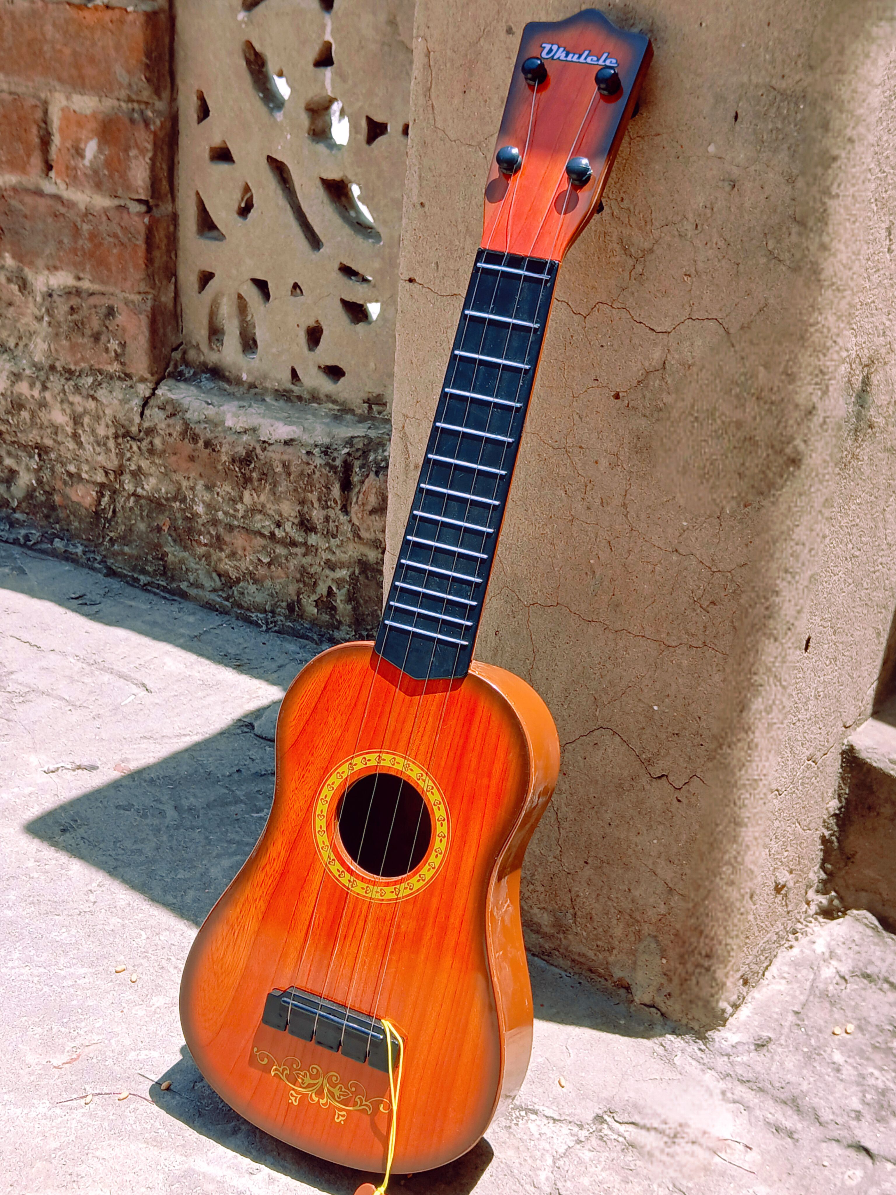 A wooden ukulele leaning against a rustic wall under bright sunlight, creating a warm and vibrant scene.