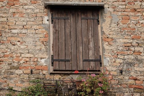 Free Charming rustic stone wall with closed wooden shutters and blooming flowers. Stock Photo