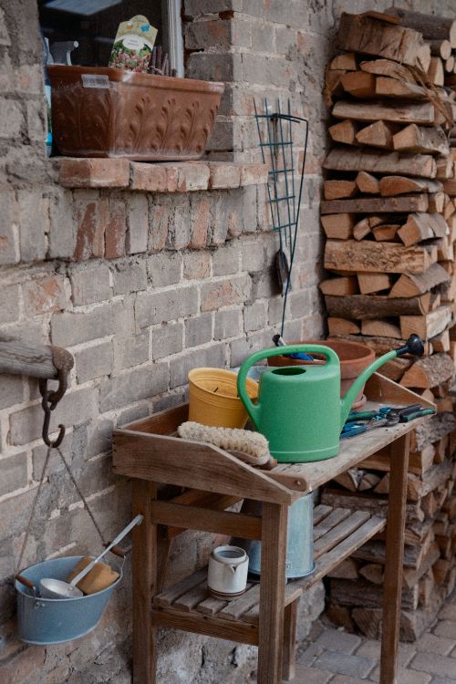 Free Rustic outdoor scene with gardening tools and stacked firewood against a brick wall. Stock Photo