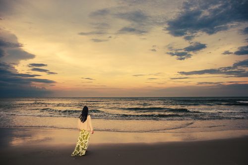Free A peaceful evening with a woman standing on Cửa Tùng Beach, Vietnam, gazing at a serene sunset. Stock Photo