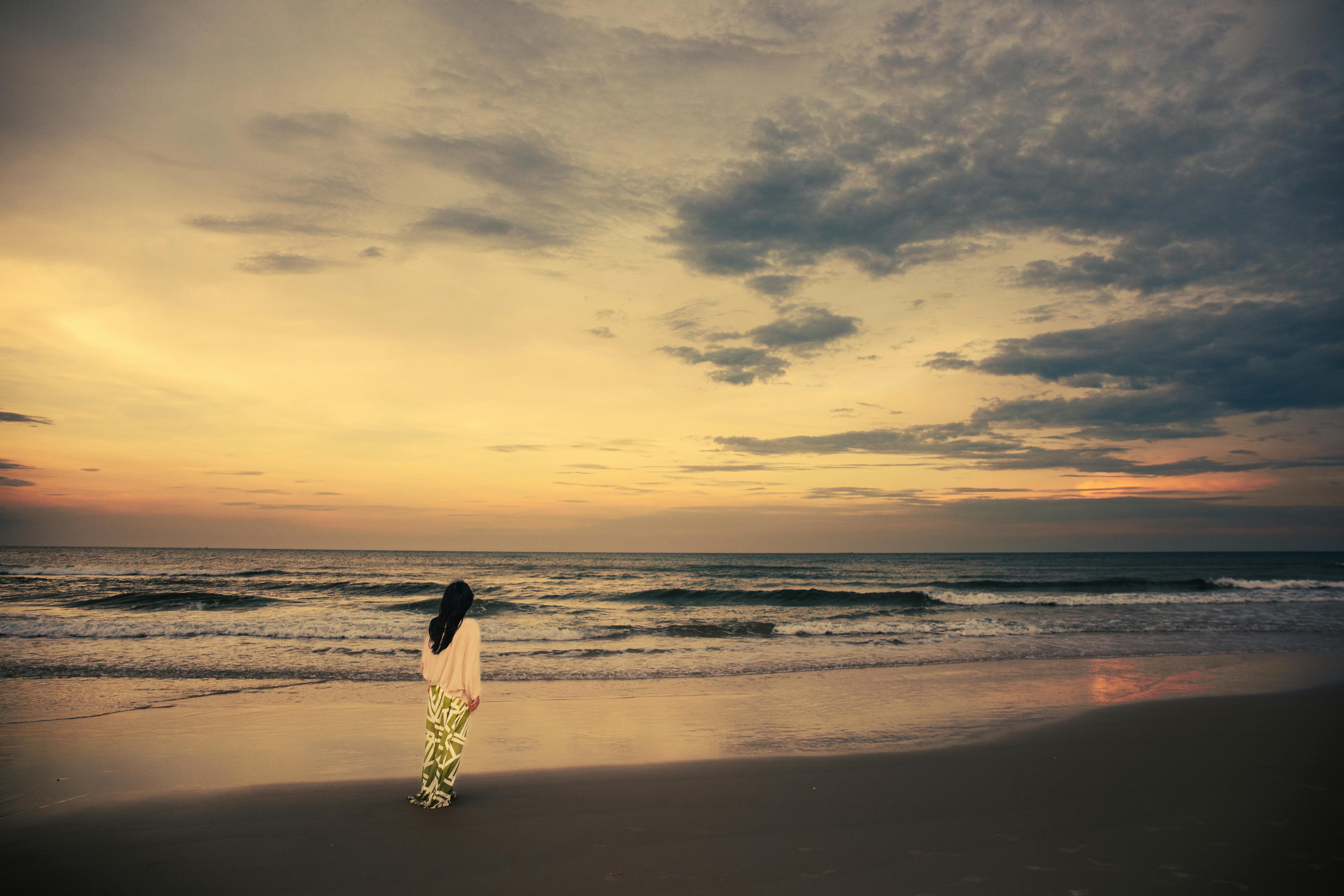 A solitary woman walks on Cửa Tùng beach at sunset, capturing tranquil ocean and vibrant sky.