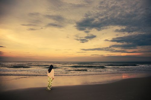 Free A solitary woman walks on Cửa Tùng beach at sunset, capturing tranquil ocean and vibrant sky. Stock Photo