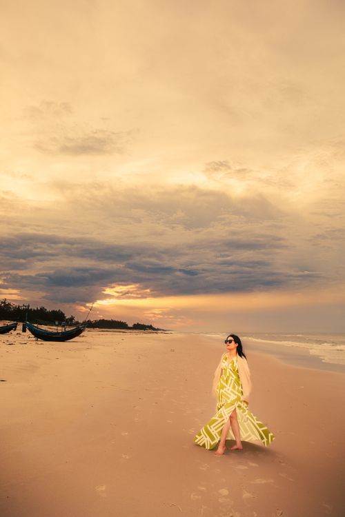 Free Elegant woman in a flowing dress walks along Cửa Tùng Beach at a serene sunset. Stock Photo
