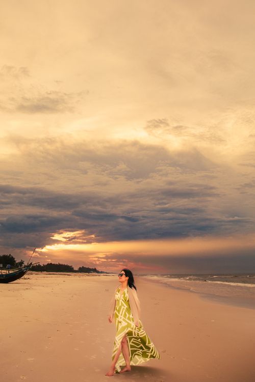 Free Woman in a green dress strolling on Cửa Tùng beach during a vibrant sunset. Captures tranquil coastal vibes. Stock Photo