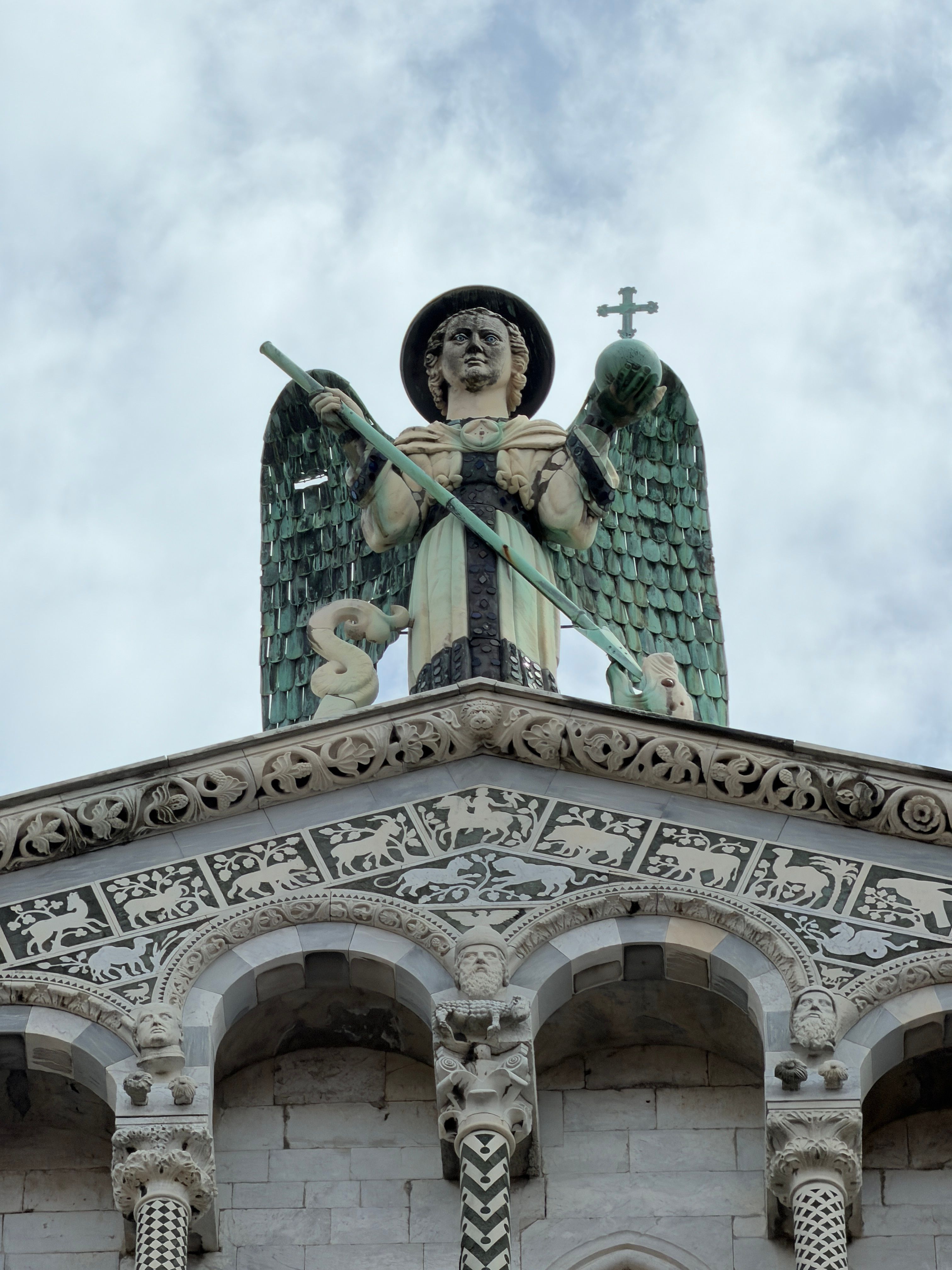 Close-up of the St Michael statue at San Michele in Foro, Lucca, against a cloudy sky.