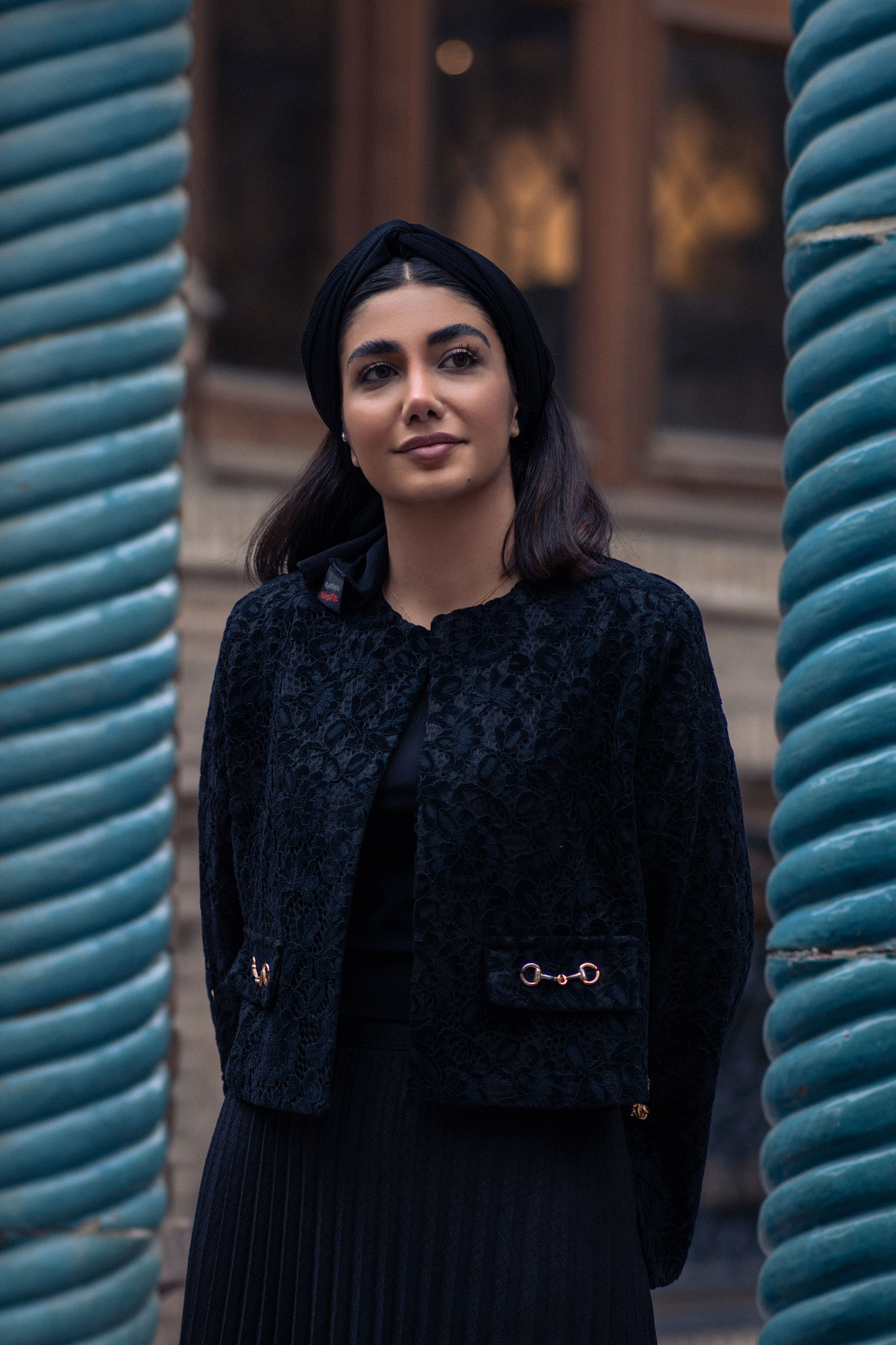 Stylish woman posing between spiraled columns in Tehran, showcasing modern Iranian fashion.