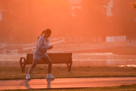 A woman jogs along a scenic park trail at sunrise, surrounded by warm golden light.