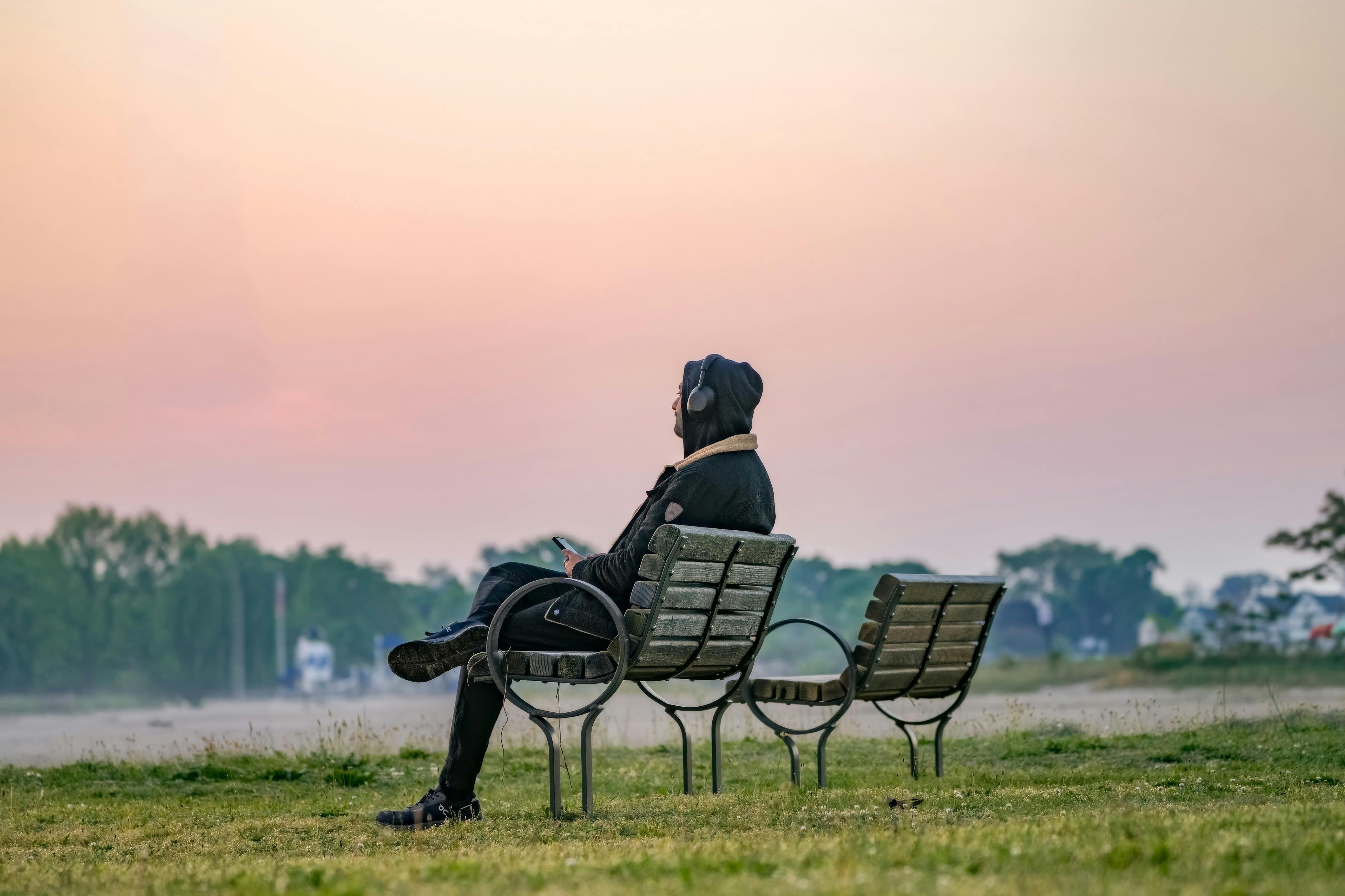 a person sitting on a park bench at sunrise, hands open, looking contemplative