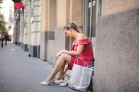 一名身穿粉色连衣裙的女子提着购物袋，坐在人行道上休息