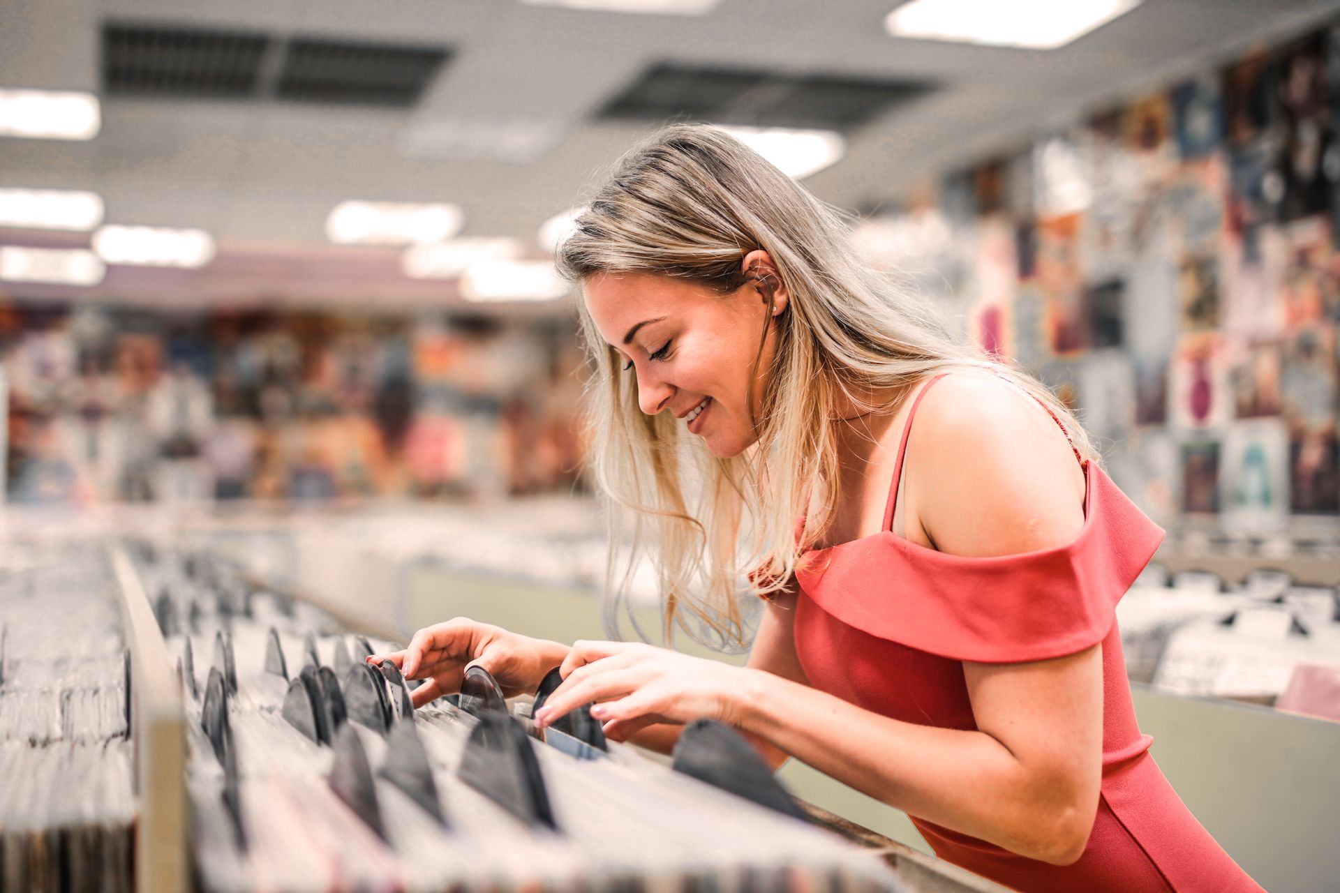 Selective Focus Photo of Smiling Woman in Pink Selecting Vinyl Records From a Music Store