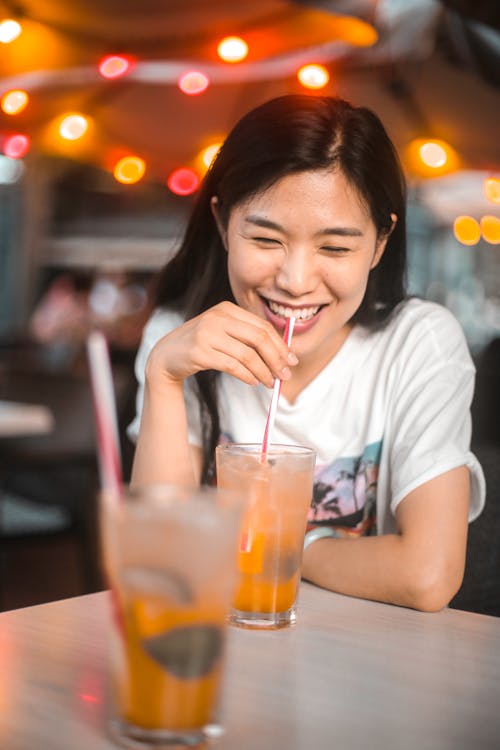 Free Cheerful ethnic woman drinking yummy beverage with ice in cafe Stock Photo