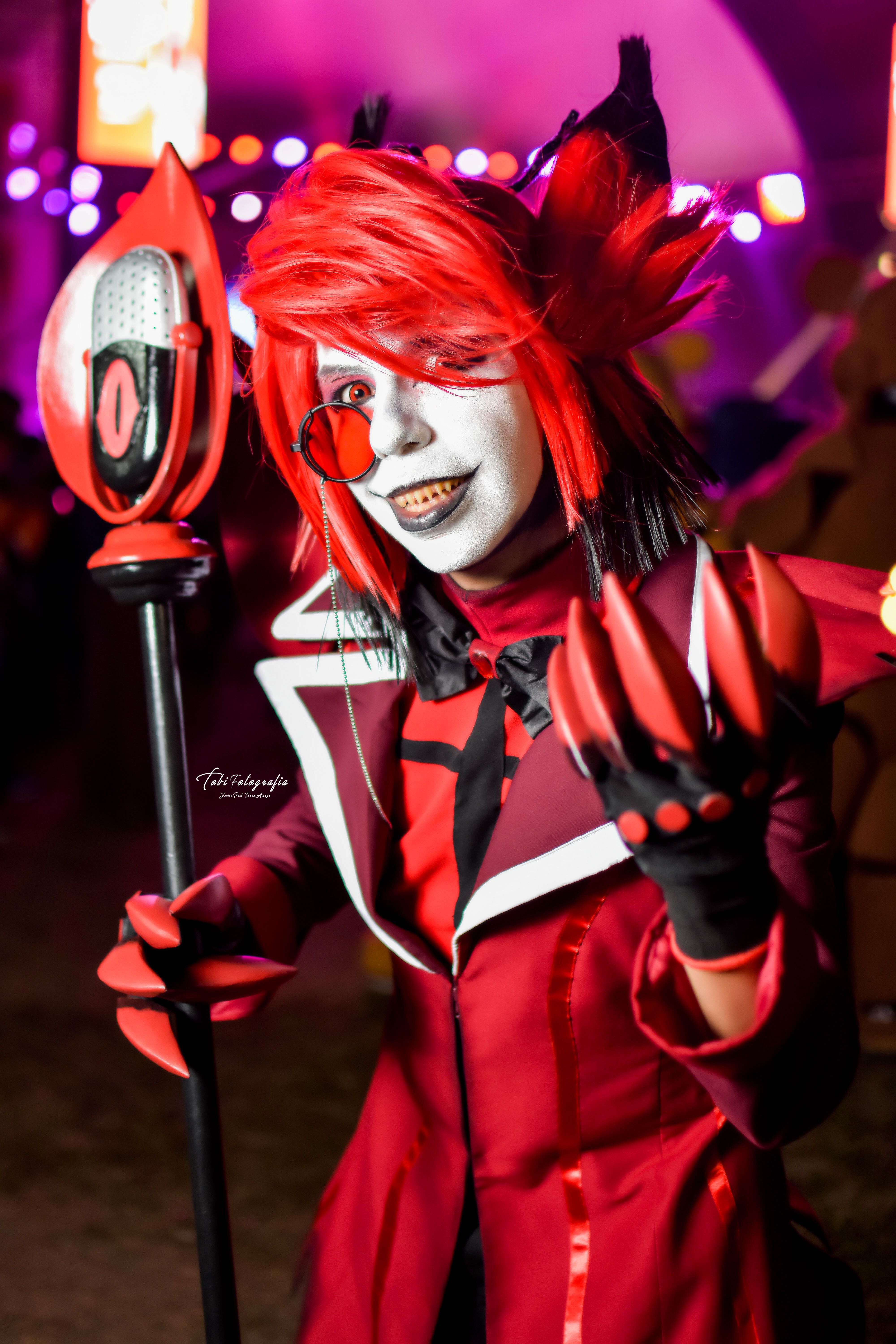 Colorful cosplay character with striking red attire and makeup at a nighttime event.