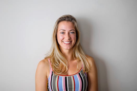 一位金发女子身穿条纹背心，在白色背景下微笑着，散发出幸福感