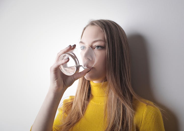 Woman Wearing Yellow Knit Sweater While Drinking Water