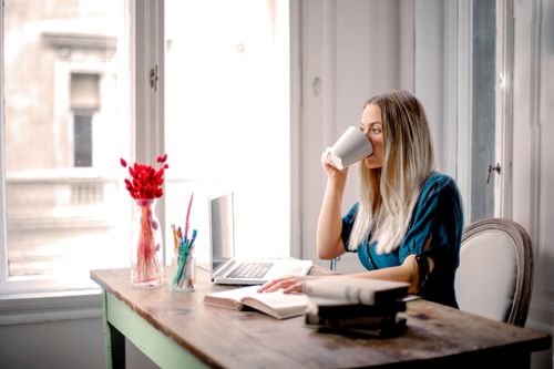 Free A woman enjoys a coffee break while working at home with her laptop and books. Stock Photo