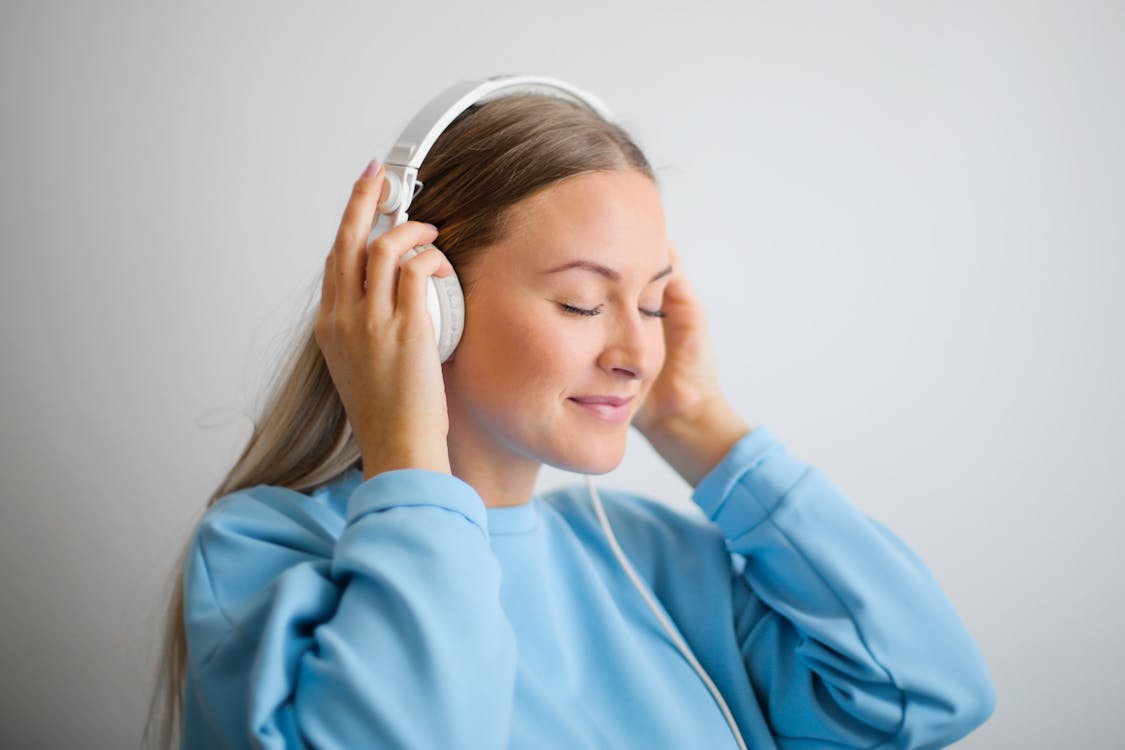 Free Portrait Photo of Woman in Blue Sweatshirt Wearing White Headphones Listening to Music Stock Photo