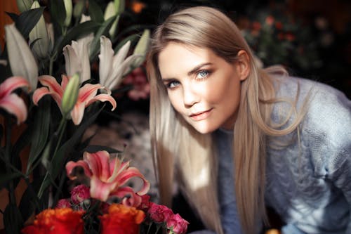 Woman in Blue Long Sleeve Shirt Standing by the Flowers