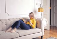 Woman in yellow sweater reading a book while enjoying coffee on a comfortable sofa.
