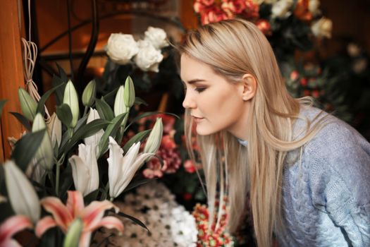 A woman in a gray sweater smells a beautiful bouquet of lilies indoors, capturing a fragrant moment.