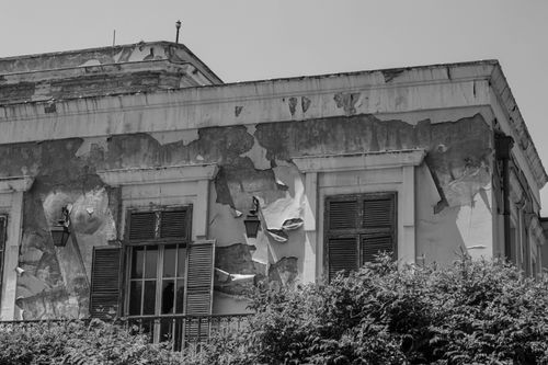 Free Black and white photo of an old building facade with peeling paint and closed shutters. Stock Photo