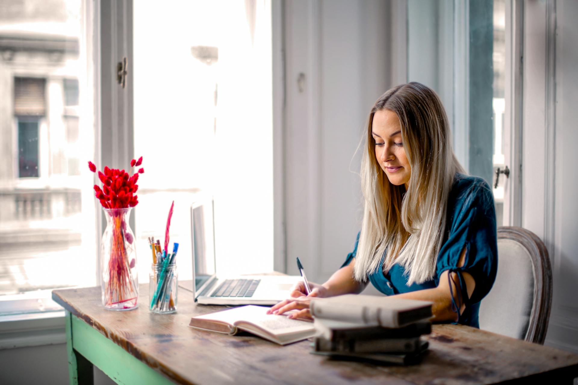 Woman in Blue Long Sleeve Shirt Sitting at the Table Working