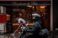 Parisian butcher shop with people and moving scooter, capturing lively street atmosphere.